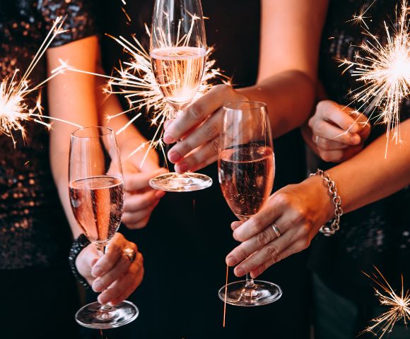 Hands holding sparklers and champagne glasses, creating a festive, celebratory atmosphere. The scene is lively with sparkling lights and bubbly drinks.