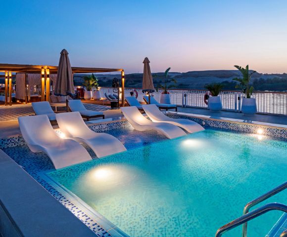 Sunset over a pool surrounded by lounge chairs and umbrellas, creating a serene and inviting atmosphere.