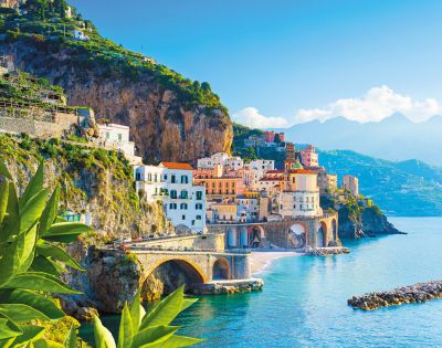 Colorful cliffside town by the sea with lemons in the foreground and mountains in the background.