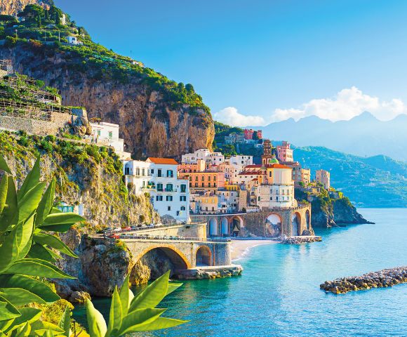 Colorful cliffside town by the sea with lemons in the foreground and mountains in the background.