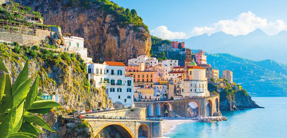 Colorful cliffside town by the sea with lemons in the foreground and mountains in the background.