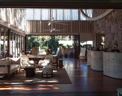 Elegant hotel lobby with open doors leading to a garden, featuring a reception desk, seating area with sofas and armchairs, and decorative lighting.