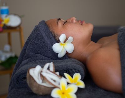 A captivating image displays a tranquil scene, where a woman lies on a dark blue towel, eyes closed, surrounded by white flowers. The images elegance shines through the blurred spa background, evoking a sense of relaxation and self-care.