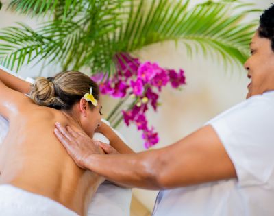A person receives a back massage from a masseuse in a spa setting, with tropical flowers and greenery in the background.