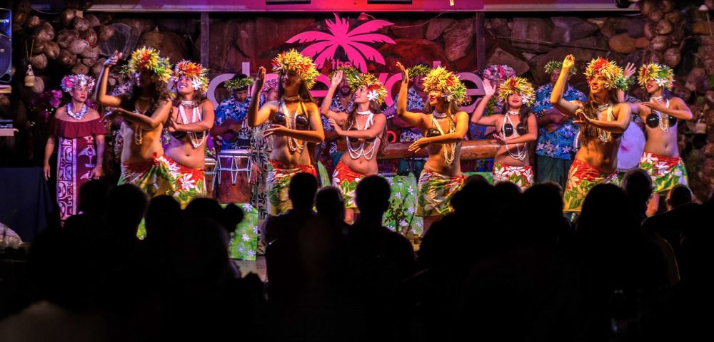 A vibrant Polynesian dance performance with dancers in floral attire and headdresses, captivating an audience in a festive atmosphere.