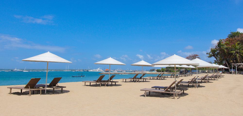 Sunny beach with lounge chairs under white umbrellas, turquoise water, and a clear blue sky. Ideal for relaxation and leisure.