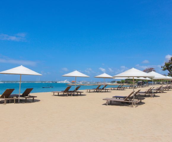 Sunny beach with lounge chairs under white umbrellas, turquoise water, and a clear blue sky. Ideal for relaxation and leisure.