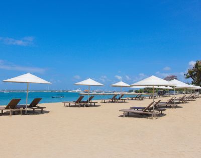 Sunny beach with lounge chairs under white umbrellas, turquoise water, and a clear blue sky. Ideal for relaxation and leisure.