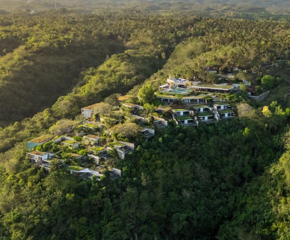Aerial view of modern hillside villas surrounded by lush, dense green forest, evoking serenity and harmony with nature. Sunny, peaceful atmosphere.