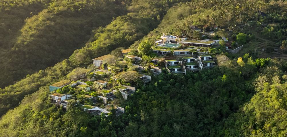 Aerial view of modern hillside villas surrounded by lush, dense green forest, evoking serenity and harmony with nature. Sunny, peaceful atmosphere.