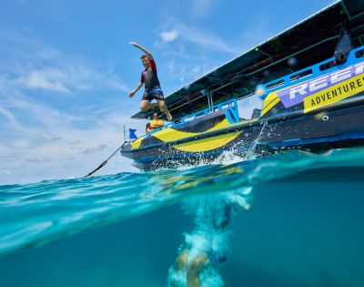 A person in swimwear jumps joyfully from a boat named 