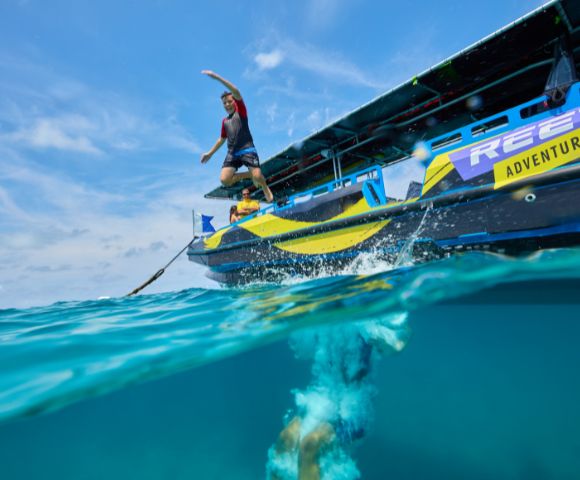A person in swimwear jumps joyfully from a boat named 