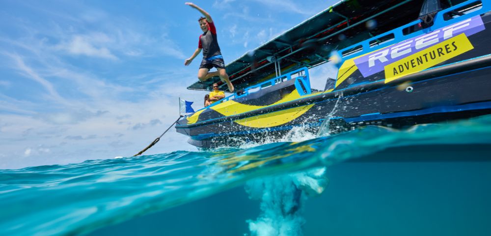 A person in swimwear jumps joyfully from a boat named 