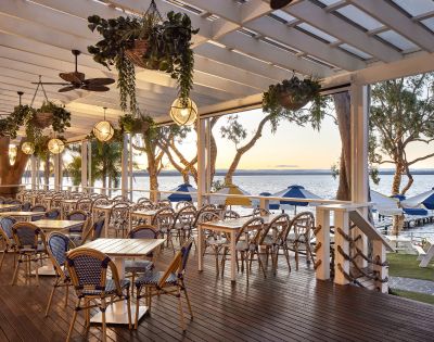 Outdoor dining setup under a pergola with hanging plants and ceiling fans.