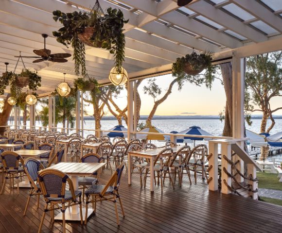 Outdoor dining setup under a pergola with hanging plants and ceiling fans.