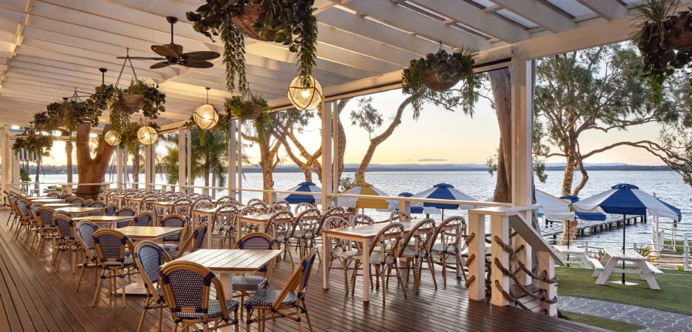 Outdoor dining setup under a pergola with hanging plants and ceiling fans.