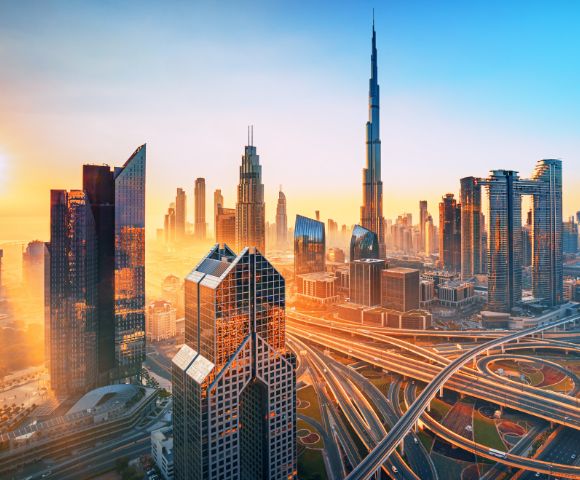 A stunning skyline of a modern city at sunrise, featuring towering skyscrapers with an intricate network of highways below, glowing in a warm golden light.
