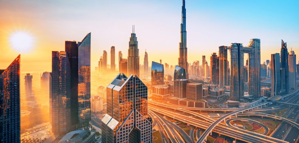 A stunning skyline of a modern city at sunrise, featuring towering skyscrapers with an intricate network of highways below, glowing in a warm golden light.