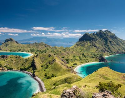 Scenic view of Komodo Island's lush green hills and turquoise bays under a clear blue sky, conveying a sense of tranquility and natural beauty.