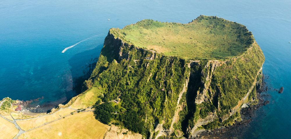 Aerial view of Jeju Island surrounded by the ocean, showcasing its lush greenery and coastal features.