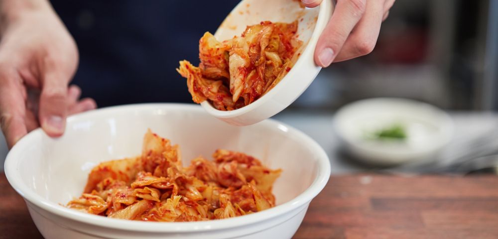 A person holds a bowl of kimchi, showcasing a delicious meal ready to be enjoyed.