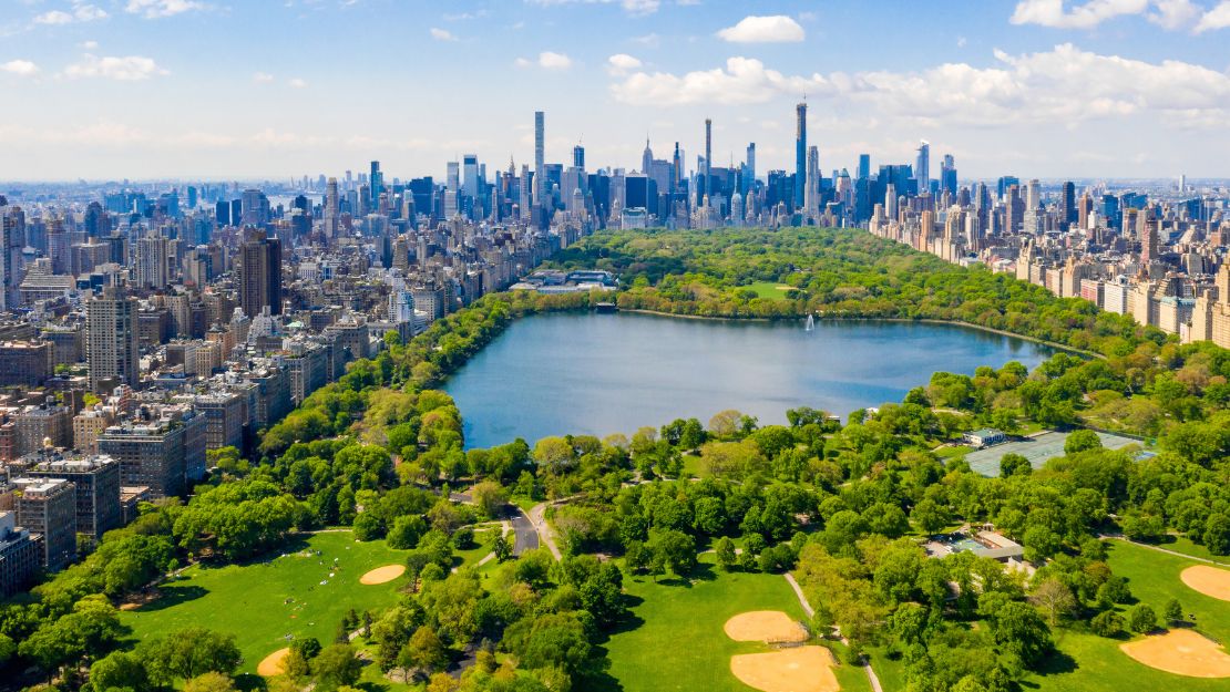 Aerial view of Central Park in New York City, surrounded by towering skyscrapers. Vibrant green trees and a large reservoir create a tranquil contrast.