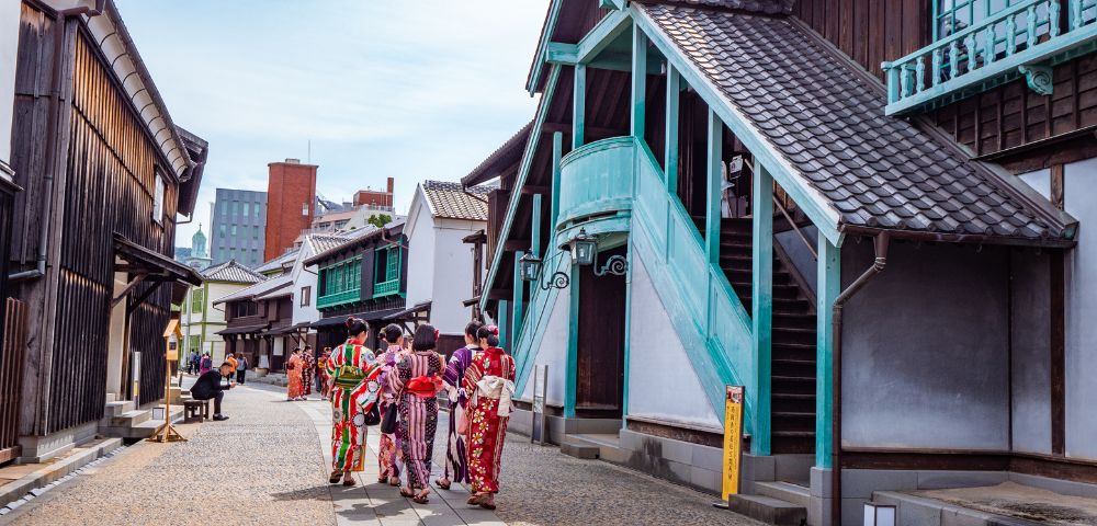 A group of people in traditional Japanese kimonos walking along a street lined with old-style wooden buildings.