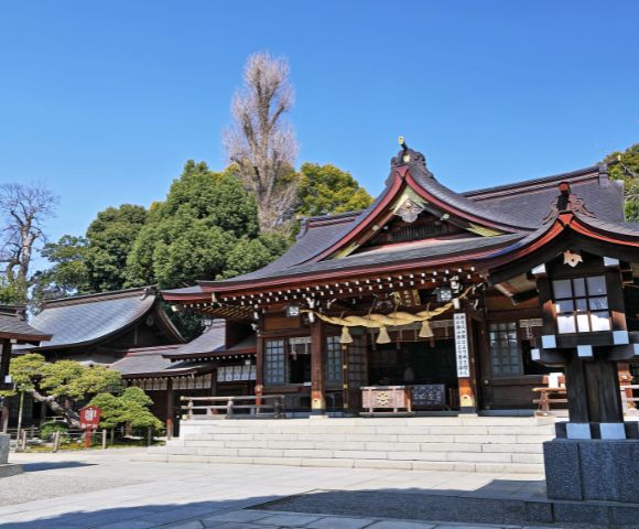 Traditional Japanese shrine with curved wooden roofs and lanterns surrounded by lush greenery.