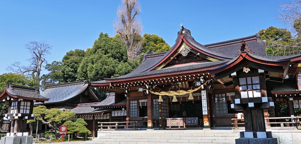 Traditional Japanese shrine with curved wooden roofs and lanterns surrounded by lush greenery.