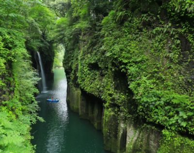 Serene gorge with a waterfall and a kayaker paddling through lush greenery.