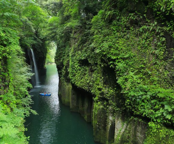 Serene gorge with a waterfall and a kayaker paddling through lush greenery.