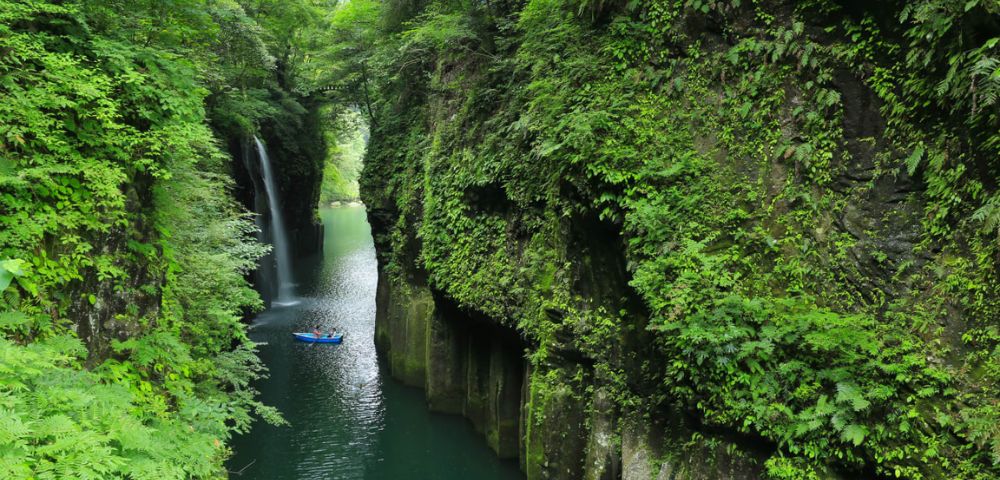 Serene gorge with a waterfall and a kayaker paddling through lush greenery.