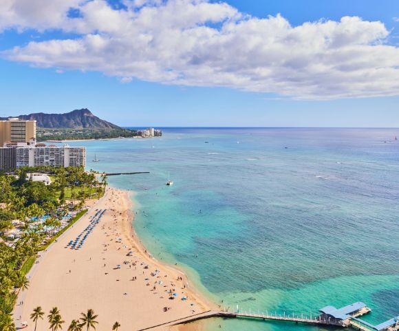 Scenic view of Waikiki Beach with Diamond Head crater, clear blue ocean, sandy shore, and high-rise buildings.