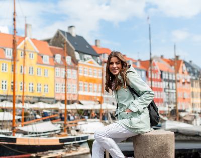 Person sitting on a stone ledge by colorful waterfront buildings and docked boats.