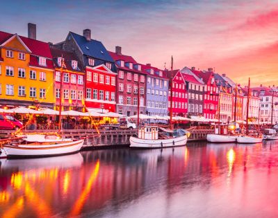 Picturesque waterfront with colorful buildings, docked boats, and a vibrant sunset sky.
