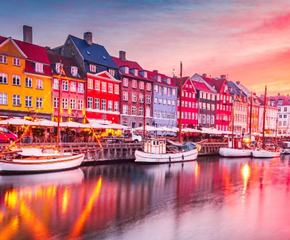 Picturesque waterfront with colorful buildings, docked boats, and a vibrant sunset sky.