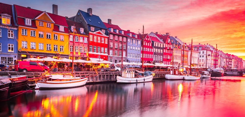 Picturesque waterfront with colorful buildings, docked boats, and a vibrant sunset sky.
