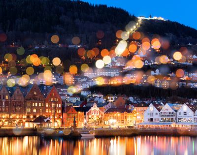Picturesque waterfront town with colorful buildings and a hilltop illuminated by blurred bokeh lights.