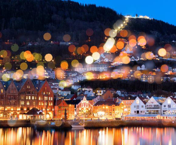Picturesque waterfront town with colorful buildings and a hilltop illuminated by blurred bokeh lights.