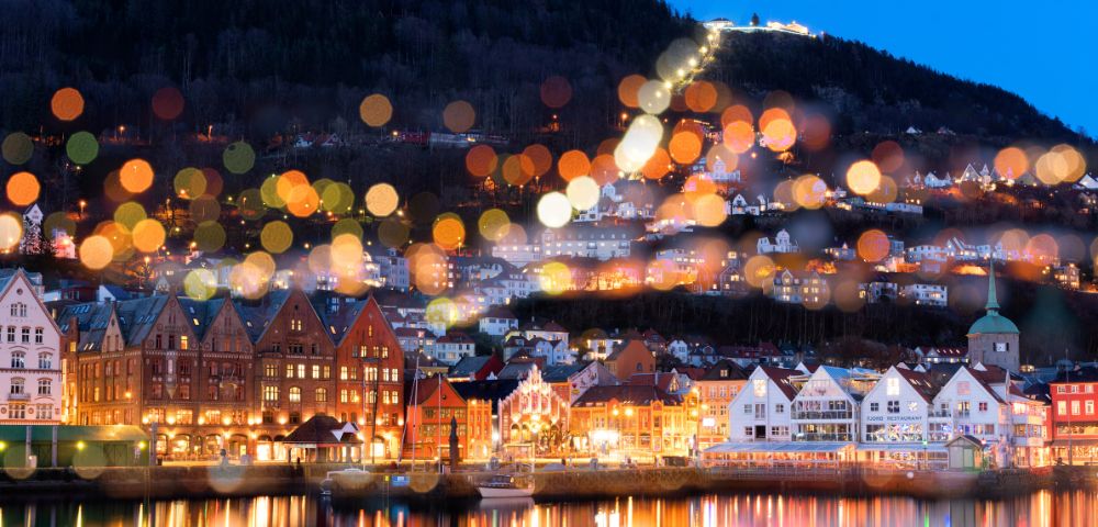 Picturesque waterfront town with colorful buildings and a hilltop illuminated by blurred bokeh lights.