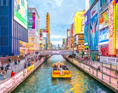 Vibrant urban canal scene with a yellow passenger boat and colorful billboards in Dotonbori, Osaka.