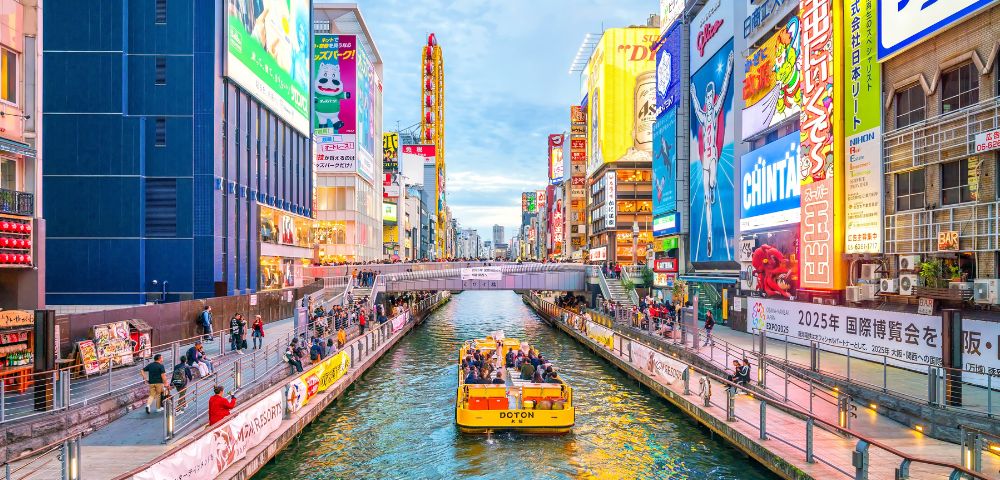 Vibrant urban canal scene with a yellow passenger boat and colorful billboards in Dotonbori, Osaka.