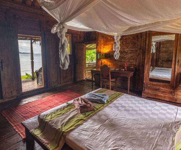 The image features a cozy bedroom with a large bed occupying the majority of the space. The bed is positioned near a window, allowing natural light to enter the room. The room also has a chair and a dining table, creating a comfortable living area. In addition to the main furniture, there are several bottles scattered around the room, possibly indicating that the occupants enjoy various beverages. A vase can also be seen, adding a touch of decoration to the space. The overall atmosphere of the room is inviting and comfortable, making it an ideal place to relax and unwind --ar 580:480 --q 2 --s 750 --v 5.2