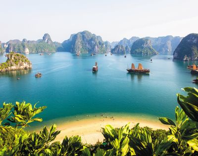 A serene view of Ha Long Bay, with traditional boats sailing through turquoise waters and limestone islands framed by lush greenery.