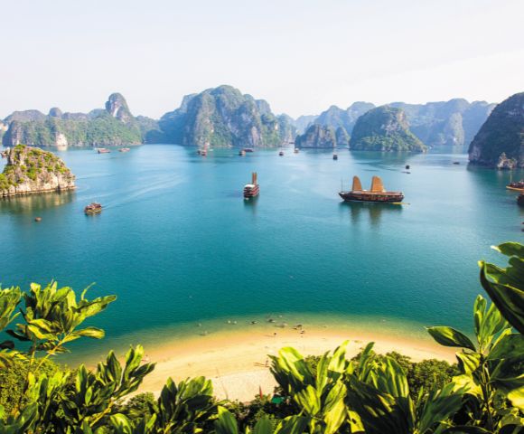 A serene view of Ha Long Bay, with traditional boats sailing through turquoise waters and limestone islands framed by lush greenery.