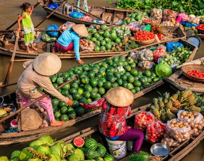 Colorful boats at a bustling market, filled with fresh produce like watermelons, pineapples, and tomatoes, with vendors in traditional hats.