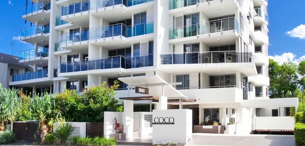 A modern multi-story apartment building with balconies and a sign labeled 