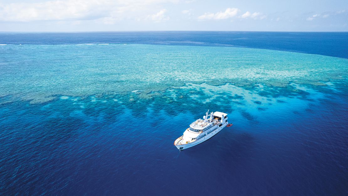 A white yacht sails in clear, turquoise waters above a vibrant coral reef.