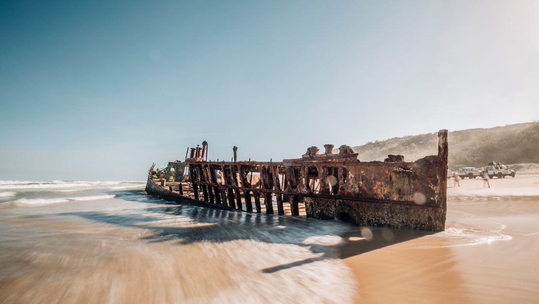 Rusty shipwreck on a sandy beach with gentle waves and a clear blue sky.