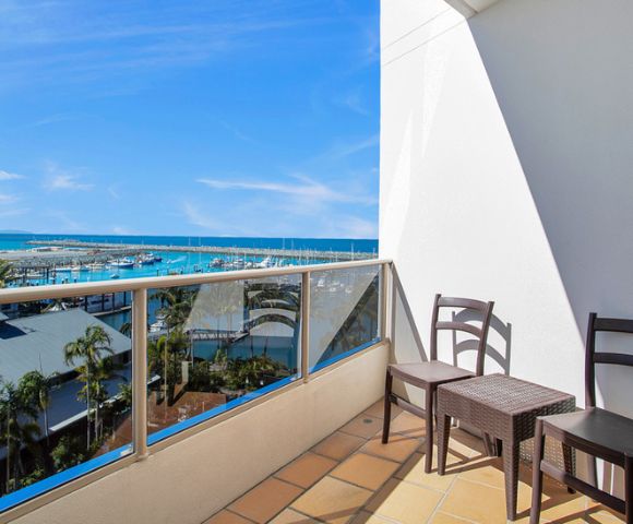 Balcony View – A balcony with a table and two chairs overlooking a peaceful landscape of water and greenery.